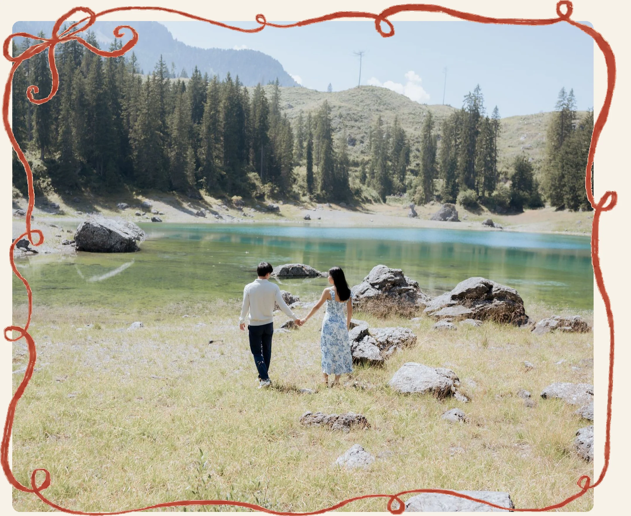 Lia and Tony walking hand in hand along the shore of a turquoise mountain lake, inside YJ’s looping red ribbon frame.